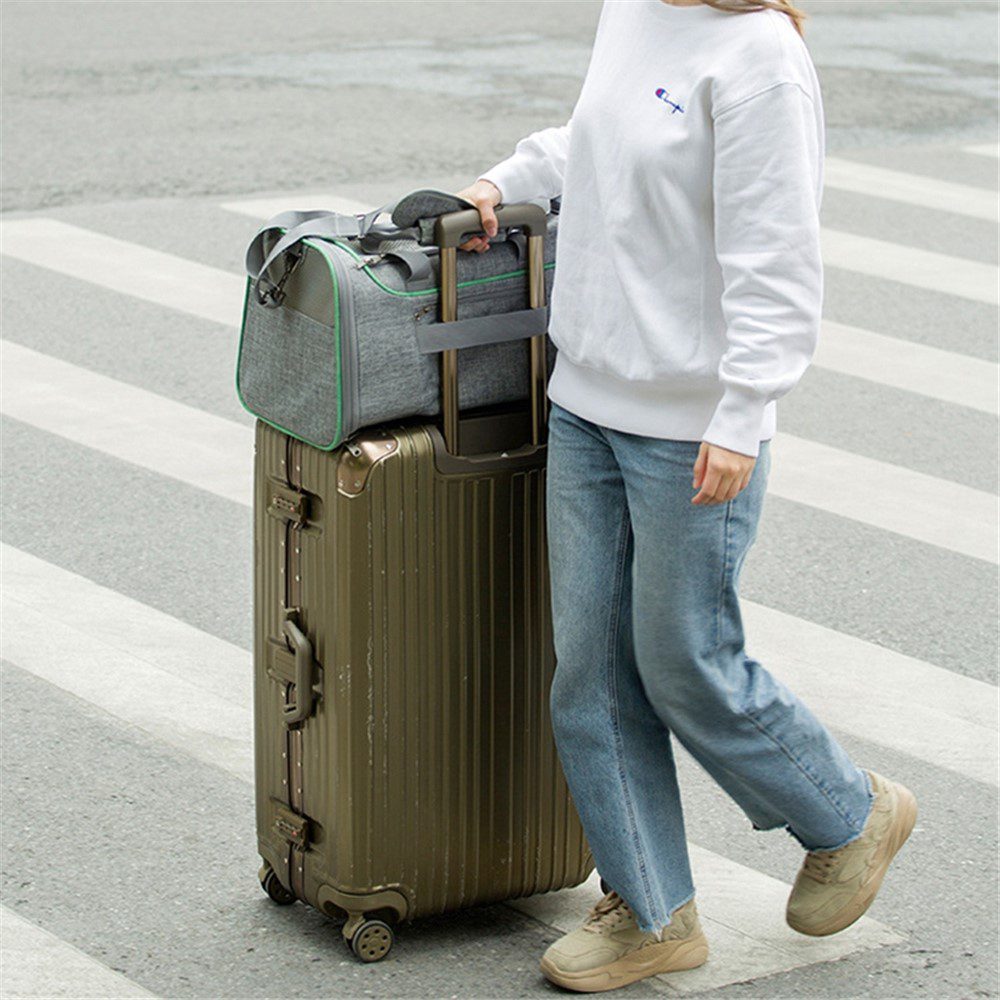 Femme traversant un passage piéton avec un sac gris glissé sur la poignée télescopique d'une valise rigide dorée