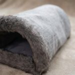 Détail de l'ouverture bordée de fourrure et du tissu gris du sac de couchage pour chat