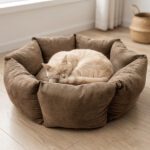 Chat crème détendu dans le panier rond ComfyNest en velours marron