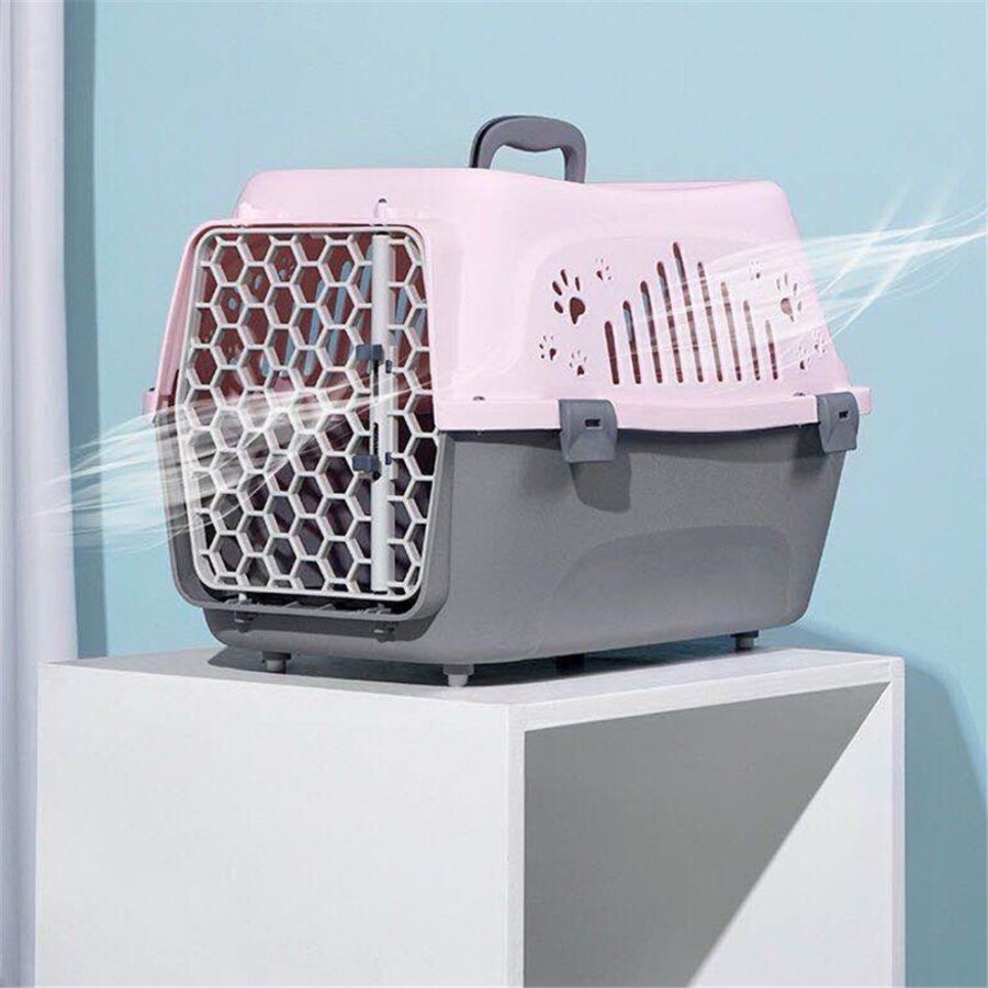 Caisse de transport rose et grise à poignée, porte grillagée en nid d'abeille, posée sur un socle blanc fond bleu