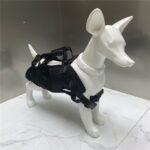 Mannequin de chien blanc portant un harnais noir avec poignée de dos et boucles de sangle, sur un sol de marbre
