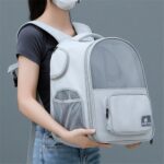 Femme portant un sac à dos de transport gris clair devant elle, tenu à deux mains, avec dôme en filet et poche avant